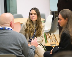 Three individuals are engaged in a conversation in a modern indoor setting.