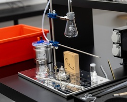 The image shows laboratory equipment including flasks and a measuring device on a black table.