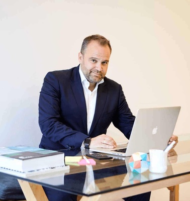 A man in a business suit working at a laptop on a desk with books and decorative plants.