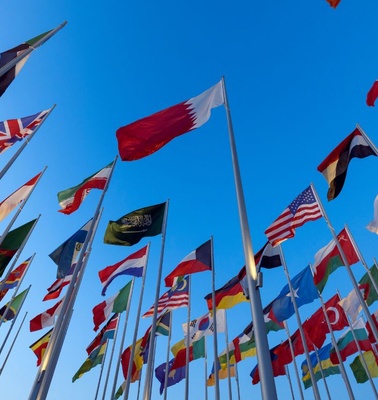 A collection of flags from various countries against a blue sky.