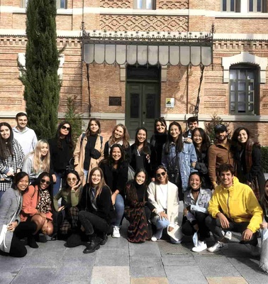 A group of diverse young people posing for a photo in front of a historic brick building with greenery.