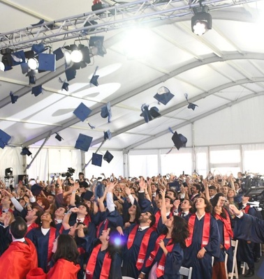 A large crowd of graduates celebrating by throwing their caps in the air inside a tent.