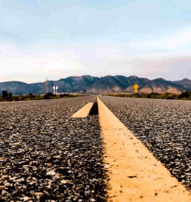 A low angle view of a long straight road leading towards mountains under a blue sky.