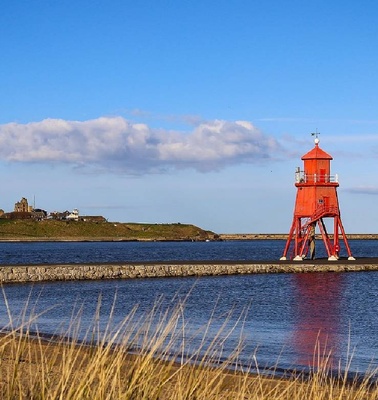 A bright red lighthouse stands on a pier by the calm waters under a clear blue sky.