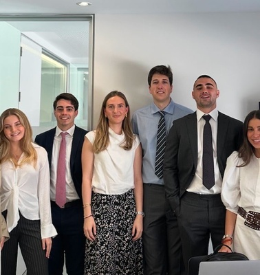 A group of eight young professionals posing together in an office environment.