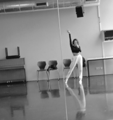 A dancer practices alone in a spacious, well-lit dance studio with mirrors and barres.