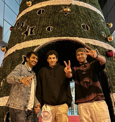 Three young men posing in front of a large decorated Christmas tree.