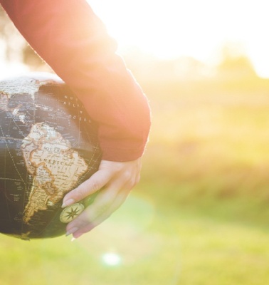 A person holding a globe in a sunlit outdoor setting.