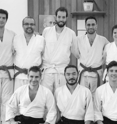 A group of nine martial artists in white karate gis posing for a photo in a dojo.