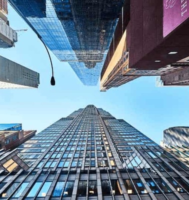 Looking upwards at a tall skyscraper surrounded by other high-rise buildings under a clear blue sky.