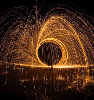 A dramatic long exposure photo capturing a person creating a circle of sparks with steel wool at night.