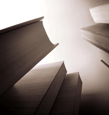 A dramatic low-angle view of several open books stacked irregularly with soft back-lighting.