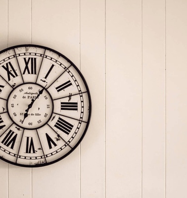 A vintage wall clock with Roman numerals on a white wooden background.