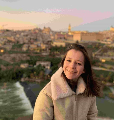 A woman smiling with a scenic cityscape and river in the background during sunset.