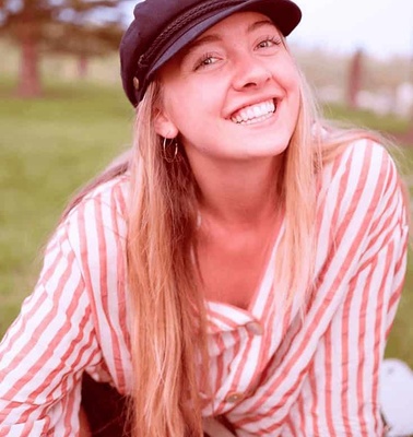 A smiling woman wearing a black cap and a striped shirt sitting outdoors.