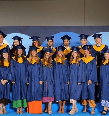 A group of graduates in blue gowns and caps posing in front of a sign that reads 'IE University'.