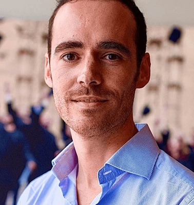 Portrait of a smiling man in a blue striped shirt with a blurred background.