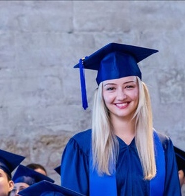 A smiling graduate in a blue cap and gown stands out among her peers during a graduation ceremony.