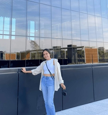 A young woman standing outside a modern building with glass facade.