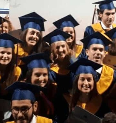 A group of graduates wearing blue and yellow caps and gowns celebrating at a graduation ceremony.