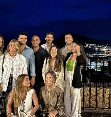 A group of eight young adults posing for a photo at night with a cityscape and lights in the background.