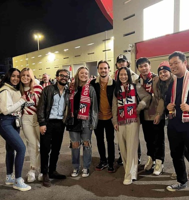 A group of people posing for a photo outside a stadium at night, some wearing sports team scarves.
