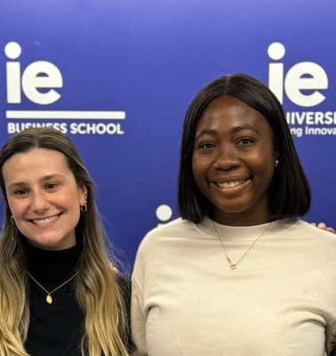 Four individuals smiling in front of a banner for IE University Business School.