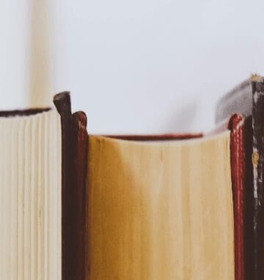 A row of old, well-used books standing upright with visible wear on the spines.