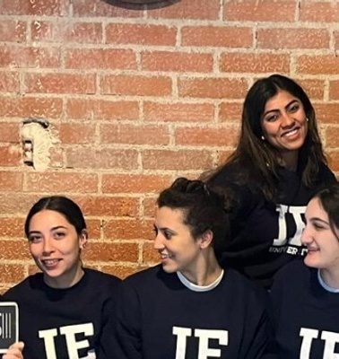 A group of six people celebrating with signs and matching navy sweatshirts in a room with a brick wall.