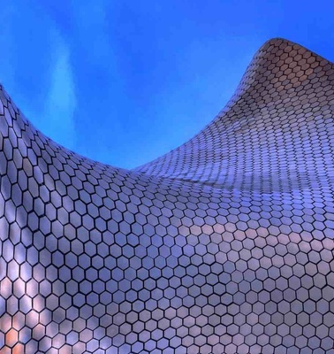 This image depicts a curved building with a hexagonal-patterned metallic facade under a blue sky.