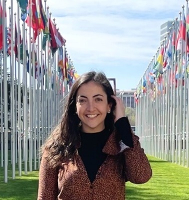 A woman smiling in front of a row of colorful vertical flags.