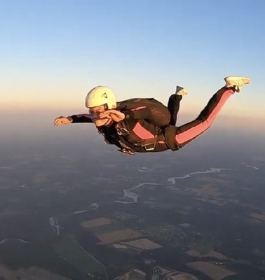 A skydiver is gracefully falling through the sky above a scenic landscape.
