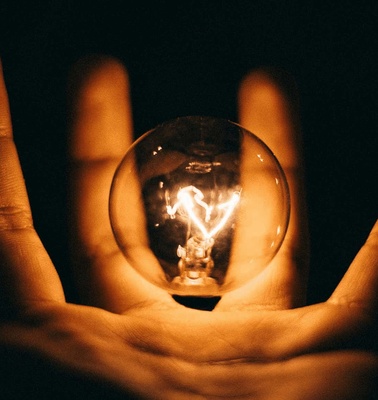 A lit light bulb held in a hand against a dark background