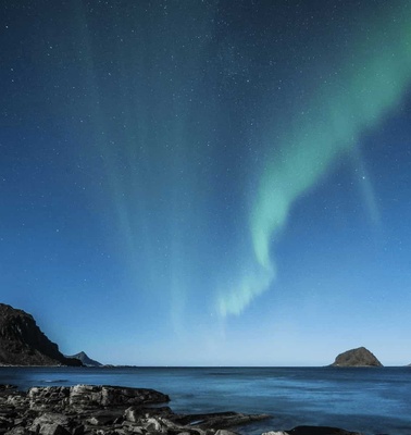 A stunning view of the Northern Lights over a serene coastal landscape at night.