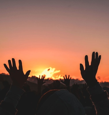 People with raised hands celebrating at sunset