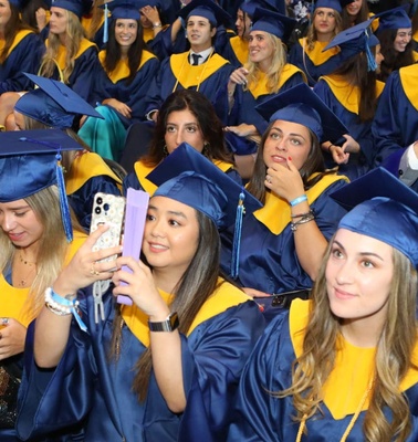 A group of students in blue and yellow graduation gowns and caps celebrating during a ceremony.