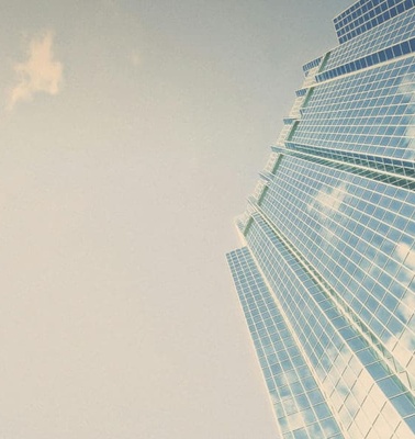 Low angle view of a modern skyscraper with reflective glass facade against a blue sky with clouds.