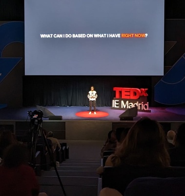 A speaker presenting at a TEDx event in a theater with audience watching attentively.