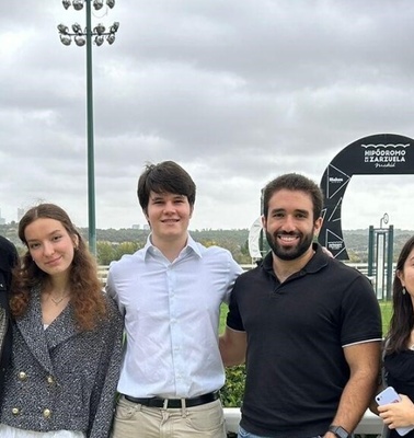 A group of six young adults posing together at a racecourse on a cloudy day.