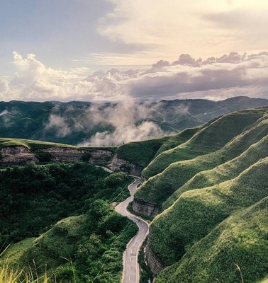 A scenic view of green hills with a winding road under a cloudy sky.