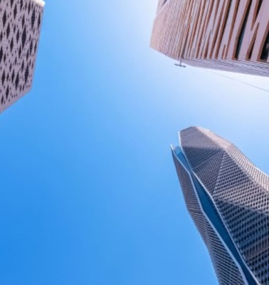 Looking up at the sky framed by towering skyscrapers with distinctive architectural designs.