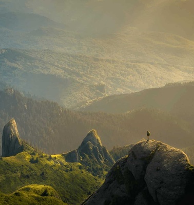 A person stands on a rock, overlooking a vast mountainous landscape bathed in golden light.