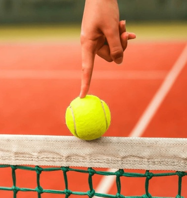 A hand balancing a tennis ball on a net at a tennis court.