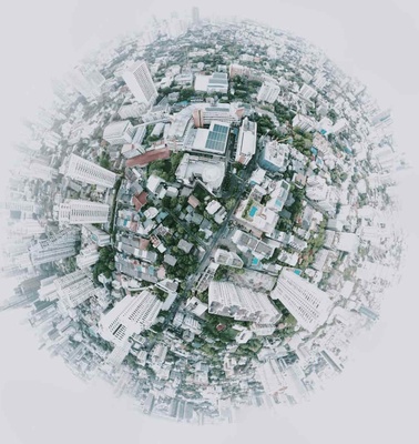 Aerial view of a cityscape manipulated into a miniature planet effect, with buildings and trees visibly wrapped around a small globe.