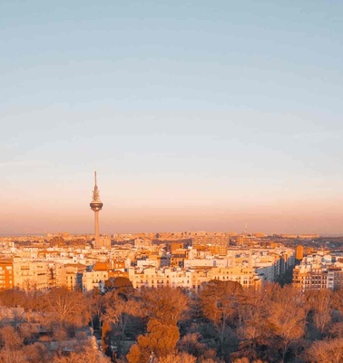 A cityscape at sunset with a distinctive tower in the background and an expansive view of buildings surrounded by trees.