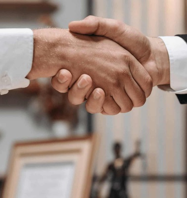 Two people in formal attire shaking hands in an office environment.