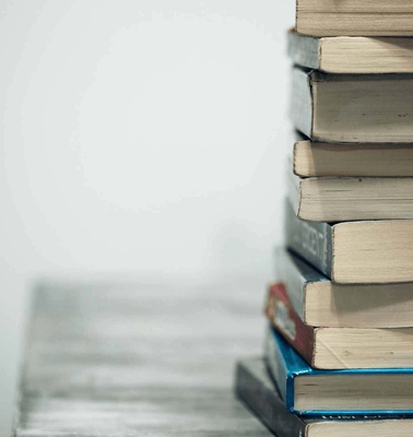 A stack of assorted books placed on a wooden surface against a blurred white background.