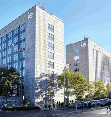 A modern urban campus with multiple buildings and pedestrians walking along the street in bright daylight.