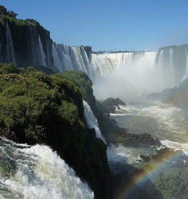 A stunning view of waterfalls surrounded by lush greenery and a rainbow in the mist.