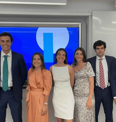 A group of six young professionals, three men and three women, dressed in business attire, standing in front of a screen displaying a desktop interface.